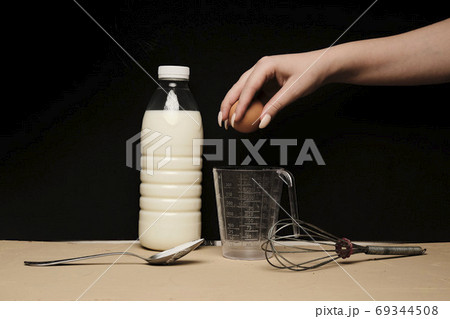 Female hands holding cracked egg over a white bowl, milk and kitchen tools on table Female hands holding cracked egg over a white bowl, milk and kitchen tools on table 69344508