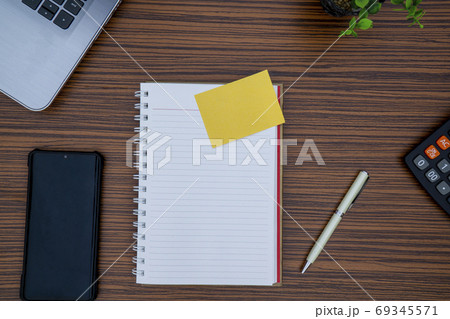 Striped brown working table with note pad, mobile phone, pen, calculator a laptop and table plant on display. 69345571