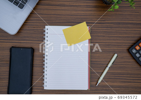 Striped brown working table with note pad, mobile phone, pen, calculator a laptop and table plant on display. 69345572