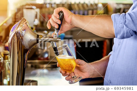 Barman pours the beer into a glass from the tap. Barman pours the beer into a glass from the tap. 69345981