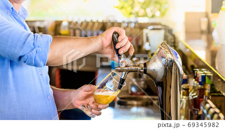 Bartender pours the beer into a glass from the tap. 69345982