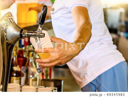 Bartender pours the beer into a glass from the tap. 69345983