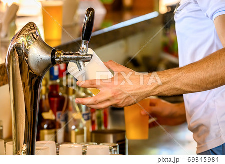 Bartender pours the cold beer into a glass from the tap. 69345984