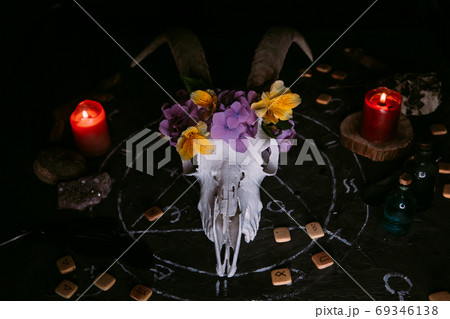 White goat scull with horns, flowers, open old book, candles on witch table. 69346138