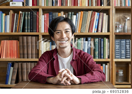 本棚の前に座るカメラ目線の若い男性 本棚の前に座るカメラ目線の若い男性 69352836