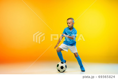 Young boy as a soccer or football player in sportwear practicing on gradient yellow studio background in neon light Young boy as a soccer or football player in sportwear practicing on gradient yellow studio background in neon light 69365824