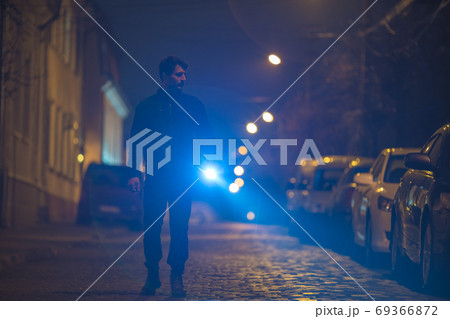 The man with a flashlight inspect the street. Evening night time The man with a flashlight inspect the street. Evening night time 69366872