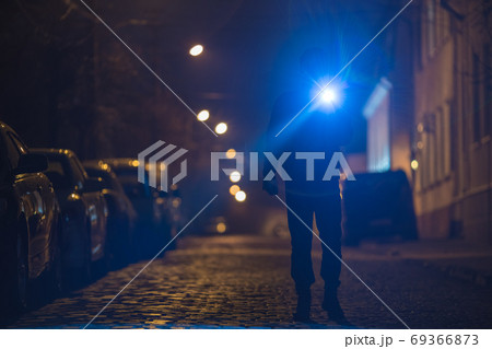 The man with a flashlight stand on wet road. Evening night time The man with a flashlight stand on wet road. Evening night time 69366873