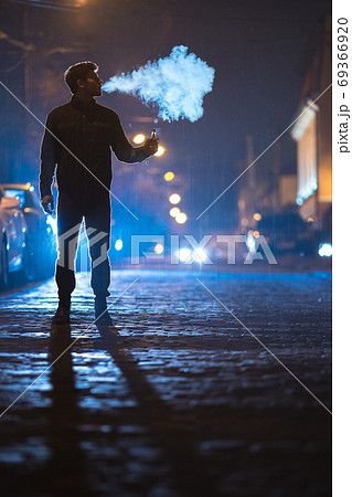 The man smoke electronic cigarette on the street. Evening night time The man smoke electronic cigarette on the street. Evening night time 69366920