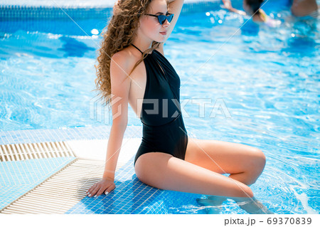 Young woman in swimsuit sitting on pool edge 69370839