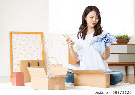 ネットショップで買った服を段ボールから出して品定めをする若い女性 ネットショップで買った服を段ボールから出して品定めをする若い女性 69373120