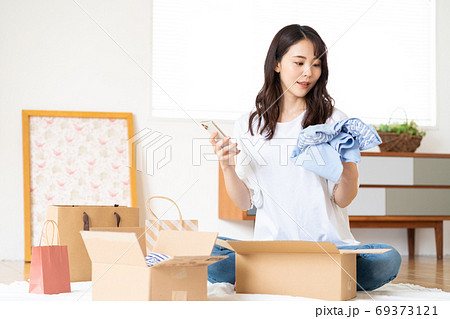 ネットショップで買った服を段ボールから出して品定めをする若い女性 ネットショップで買った服を段ボールから出して品定めをする若い女性 69373121
