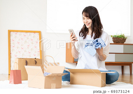 ネットショップで買った服を段ボールから出して品定めをする若い女性 69373124