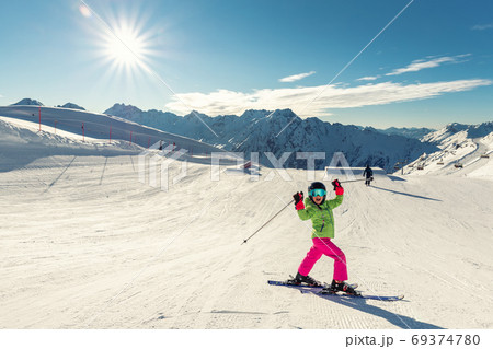 Active confident preschooler caucasian kid girl portrait with ski in helmet, goggles and bright suit enjoy winter extreme sport activities. Little child skiing on luxury alpine resort in mountains 69374780