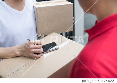 Asian delivery man in red uniform delivering parcel box to woman recipient at home 69375822