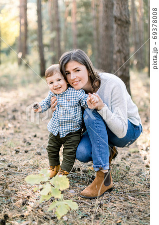 Outdoor autumn portrait of young pretty woman mother posing in autumn pine forest with her lovely cute little son, laughing together. 69378008