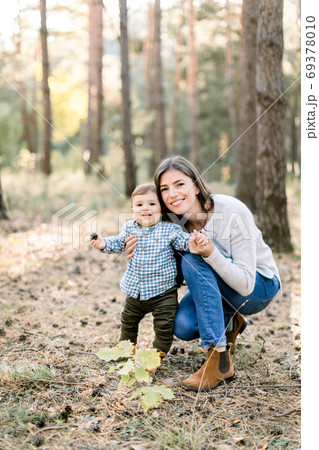 Outdoor autumn portrait of young pretty woman mother posing in autumn pine forest with her lovely cute little son, laughing together. 69378010