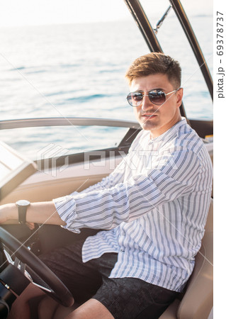 Aspirational successful businessman standing by luxury boats and yachts against a deep blue sky, holding his jacket over his shoulder. 69378737