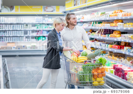 male and female shoppers push cart with grocery products in supermarket aisle male and female shoppers push cart with grocery products in supermarket aisle 69379366