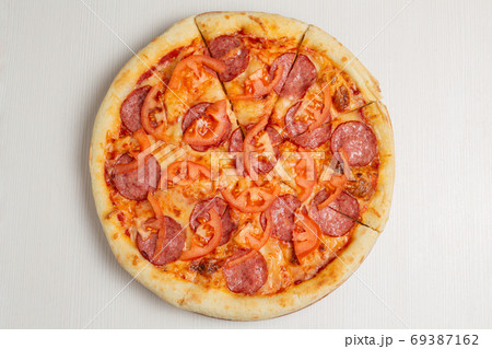 italian pizza with salami sausage, tomato and cheese, on a white wooden table 69387162