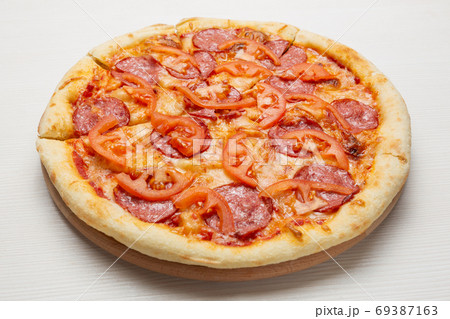 italian pizza with salami sausage, tomatoes and cheese, on a white wooden table 69387163