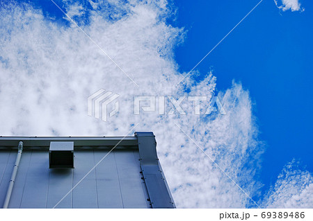 排気ダクトのある建物の外壁と白い雲が浮かぶ青空 69389486