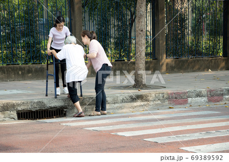 Tired asian senior woman with walker trying to climb the sidewalk after cross the road on crosswalk,facing the difficulties,barrier,tall footpath,different level floor, problems of disabled elderly 69389592