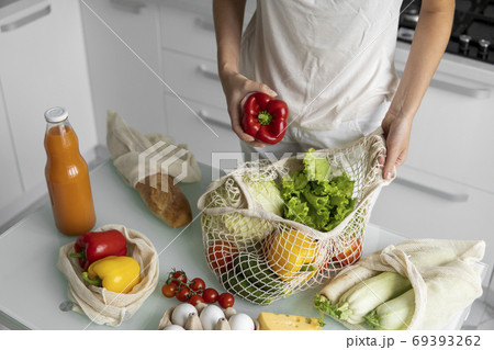 Woman hand holding Reusable eco textile grocery bag with vegetables and takes red and yellow pepper out. Zero waste and plastic free concept. Girl is holding mesh cotton shopper with vegetables. Woman hand holding Reusable eco textile grocery bag with vegetables and takes red and yellow pepper out. Zero waste and plastic free concept. Girl is holding mesh cotton shopper with vegetables. 69393262