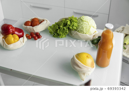 Vegetables, fruits in reusable eco cotton bags and orange juice in a glass bottle on table. Zero waste shopping concept. Multi-use, reuse, recycle. Eco friendly canvas grocery bag. Vegetables, fruits in reusable eco cotton bags and orange juice in a glass bottle on table. Zero waste shopping concept. Multi-use, reuse, recycle. Eco friendly canvas grocery bag. 69393342