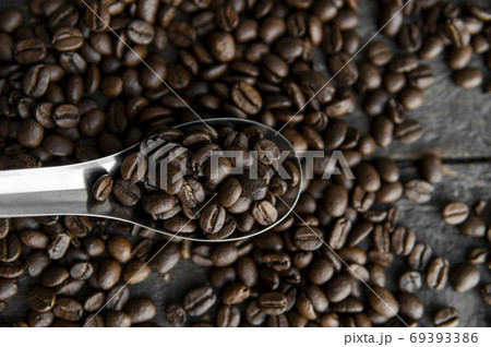 Fresh roasted arabica coffee beans in a metal spoon and scattered coffee beans on a wooden table. Fresh roasted arabica coffee beans in a metal spoon and scattered coffee beans on a wooden table. 69393386