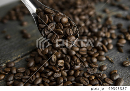 Fresh roasted arabica coffee beans in a metal spoon and scattered coffee beans on a wooden table. 69393387