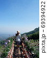 Young tourist woman on the wooden terrace with flowers, looking at mountain landscape with blue sky. 69394922