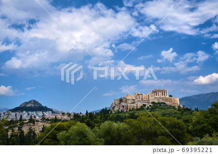 Iconic view of Acropolis hill and Lycabettus hill in background in Athens, Greece from Pnyx hill in summer daylight with great clouds in blue sky. Iconic view of Acropolis hill and Lycabettus hill in background in Athens, Greece from Pnyx hill in summer daylight with great clouds in blue sky. 69395221