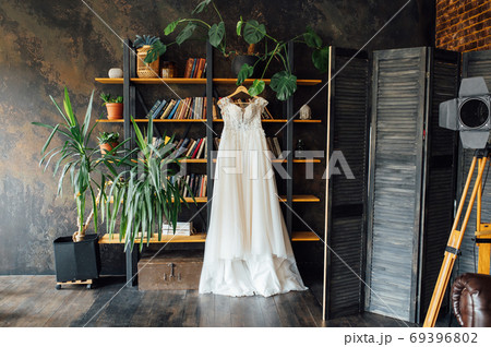 A chic silk wedding dress hangs on a bookcase. 69396802