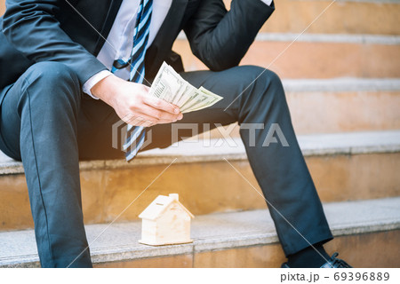 Man's hand is planning savings money to buy a home concept.Businessman keep dollar money in hand and think about the future house..Sad fired businessman sitting on the floor after failure and layoff. 69396889