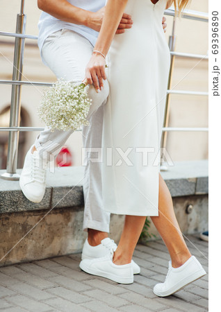 A loving couple in white clothes and sneakers hugs with their hands 69396890