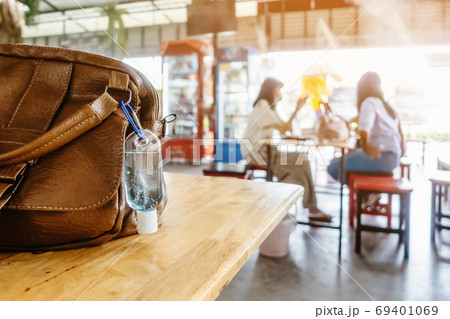 Mini portable alcohol gel bottle to kill Corona Virus(Covid-19) hang on a leather shoulder bag of a woman on table at cafeteria. New normal lifestyle.Selective focus on alcohol gel 69401069