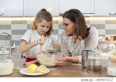Mother and daughter child together at home kitchen preparing cookies Mother and daughter child together at home kitchen preparing cookies 69407212
