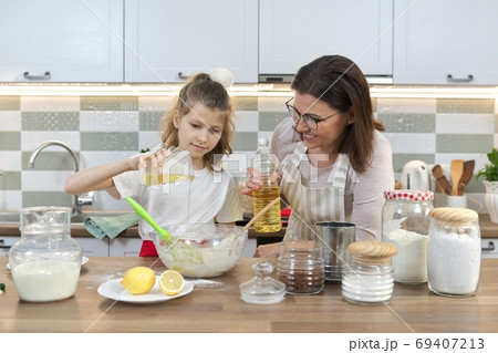 Mother and daughter child together at home kitchen preparing cookies Mother and daughter child together at home kitchen preparing cookies 69407213