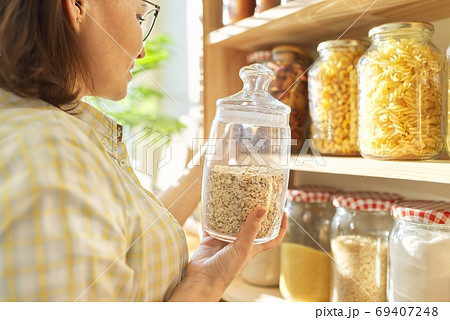 Food storage in pantry, woman holding jar of oatmeal in hand Food storage in pantry, woman holding jar of oatmeal in hand 69407248