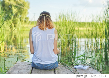 Young woman sitting with her back on wooden pier, copy space Young woman sitting with her back on wooden pier, copy space 69408204
