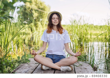Teen girl sitting in lotus position, meditating on nature Teen girl sitting in lotus position, meditating on nature 69408330