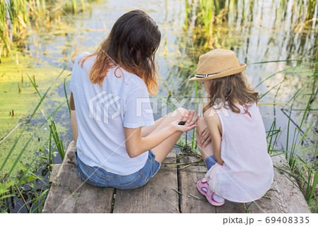 Children resting near the water on summer day, playing with water snails, back view Children resting near the water on summer day, playing with water snails, back view 69408335