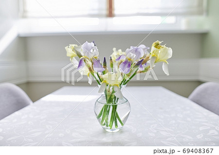 Vase with bouquet of yellow and purple irises on table near the window 69408367