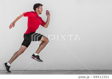 Running man runner training doing outdoor city run sprinting along wall background. Urban healthy active lifestyle. Male athlete doing sprint hiit high intensity interval training. 69411501