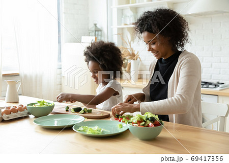 Smiling young african ethnicity woman cooking with small daughter. Smiling young african ethnicity woman cooking with small daughter. 69417356