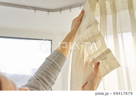 Close up of woman hands hanging curtain with metal hooks on ceiling ledge 69417679