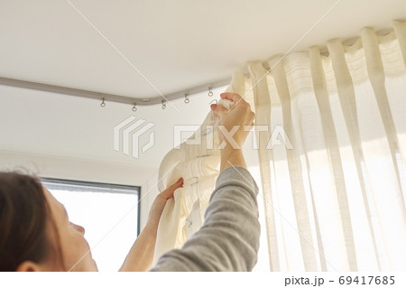Close up of woman hands hanging curtain with metal hooks on ceiling ledge 69417685