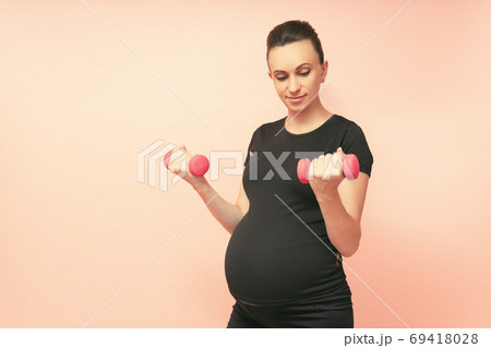 Young pregnant woman exercises with dumbell. Working out and fitness on last months of pregnancy and Young pregnant woman exercises with dumbell. Working out and fitness on last months of pregnancy and 69418028