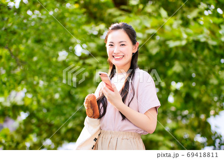 公園でスマホを持つ買い物帰りの若い女性 公園でスマホを持つ買い物帰りの若い女性 69418811